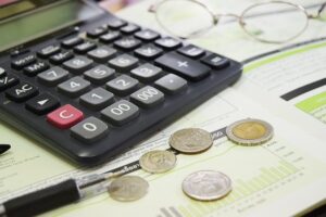 Na stole leży kalkulator, okulary, długopis i pieniądze w bilonie