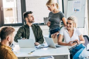 Pracownicy dobrze oświetlonego biura dyskutują przy stole, na którym stoją dwa laptopy